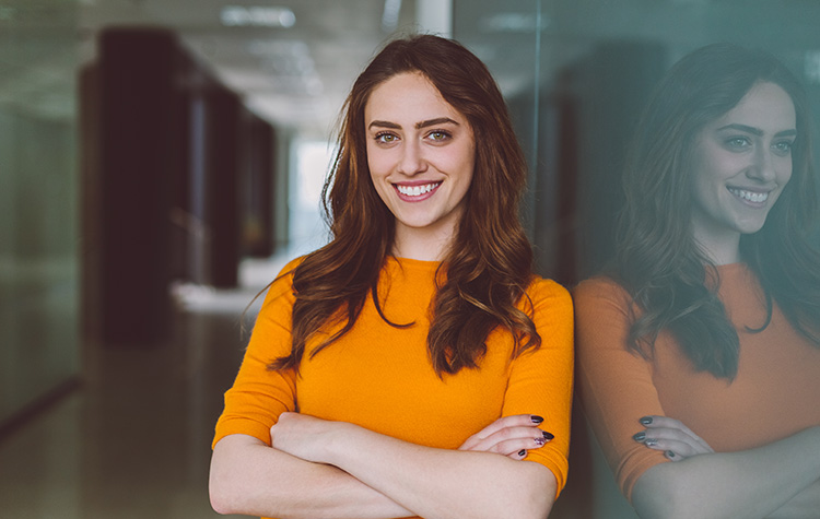 A young woman in an orange jumper looks at the camera