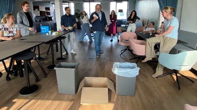 Mitarbeitende schmeißen spielerisch Müll in den Abfallkorb