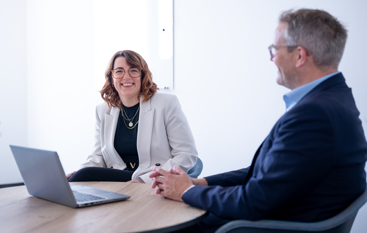 Zwei Kollegen sitzen zusammen vor einem Laptop und lachen