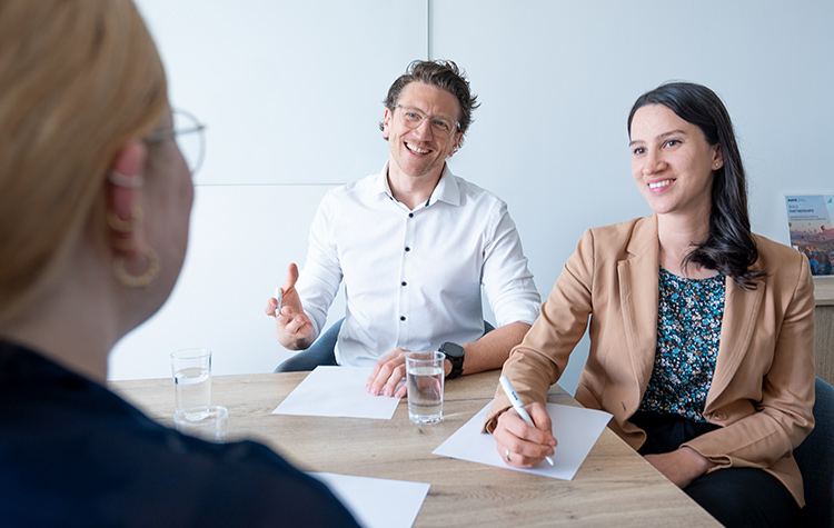 Drei Mitarbeitende sitzen in einem Meeting und unterhalten sich